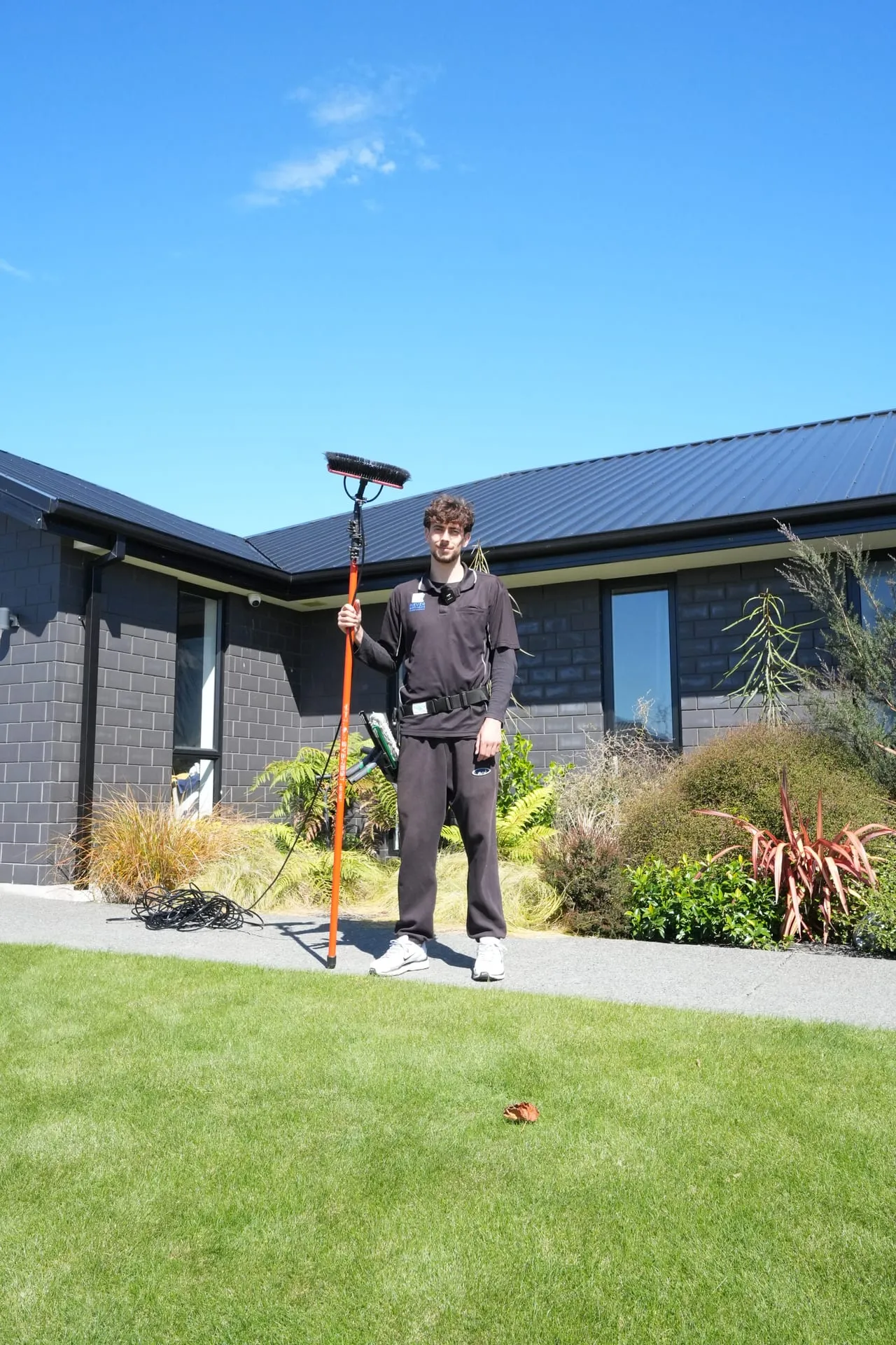 A Never Dirty Again window cleaner with a water-fed pole outside a Christchurch home
