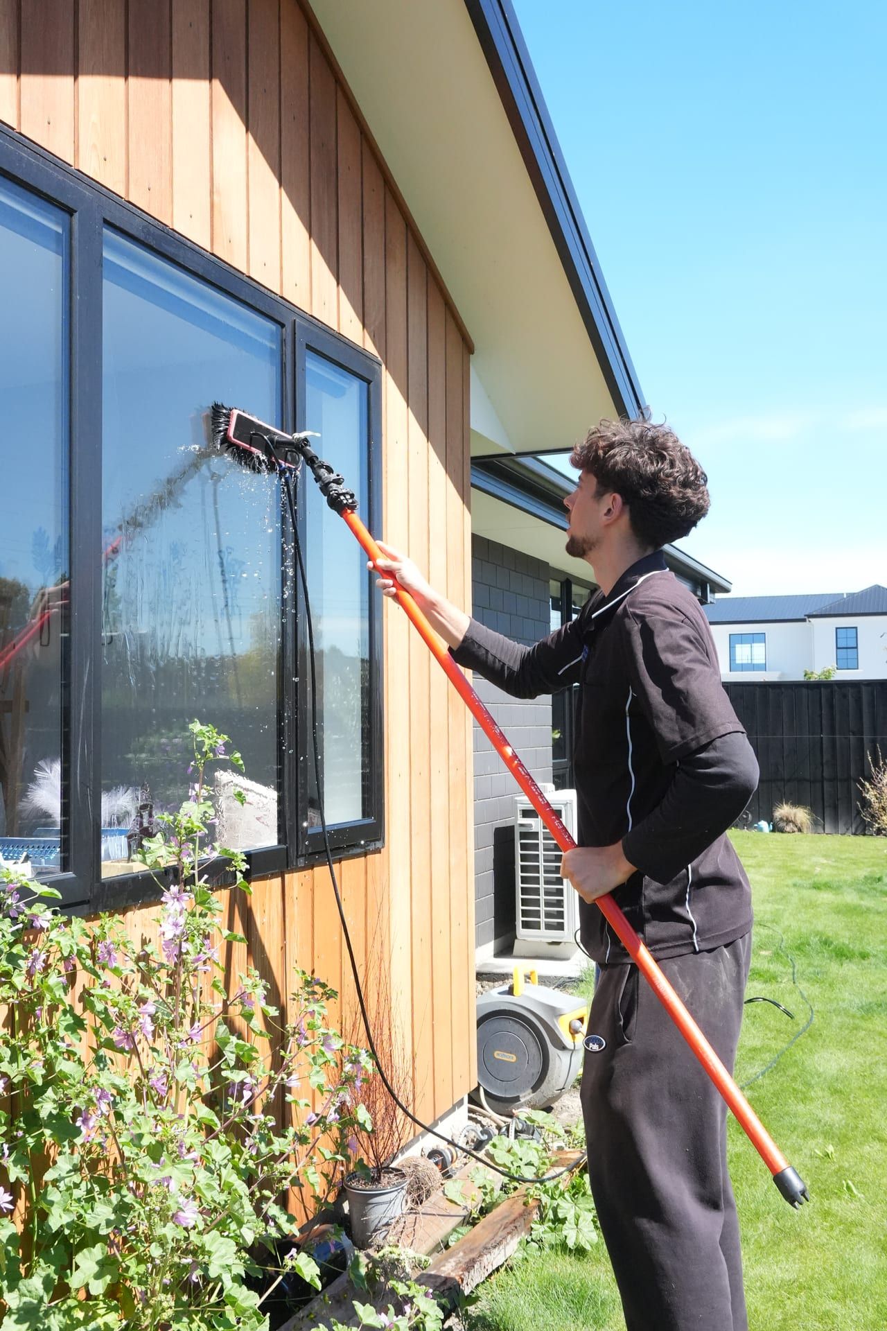 Water-fed pole cleaning a window on a cedar-clad Christchurch home