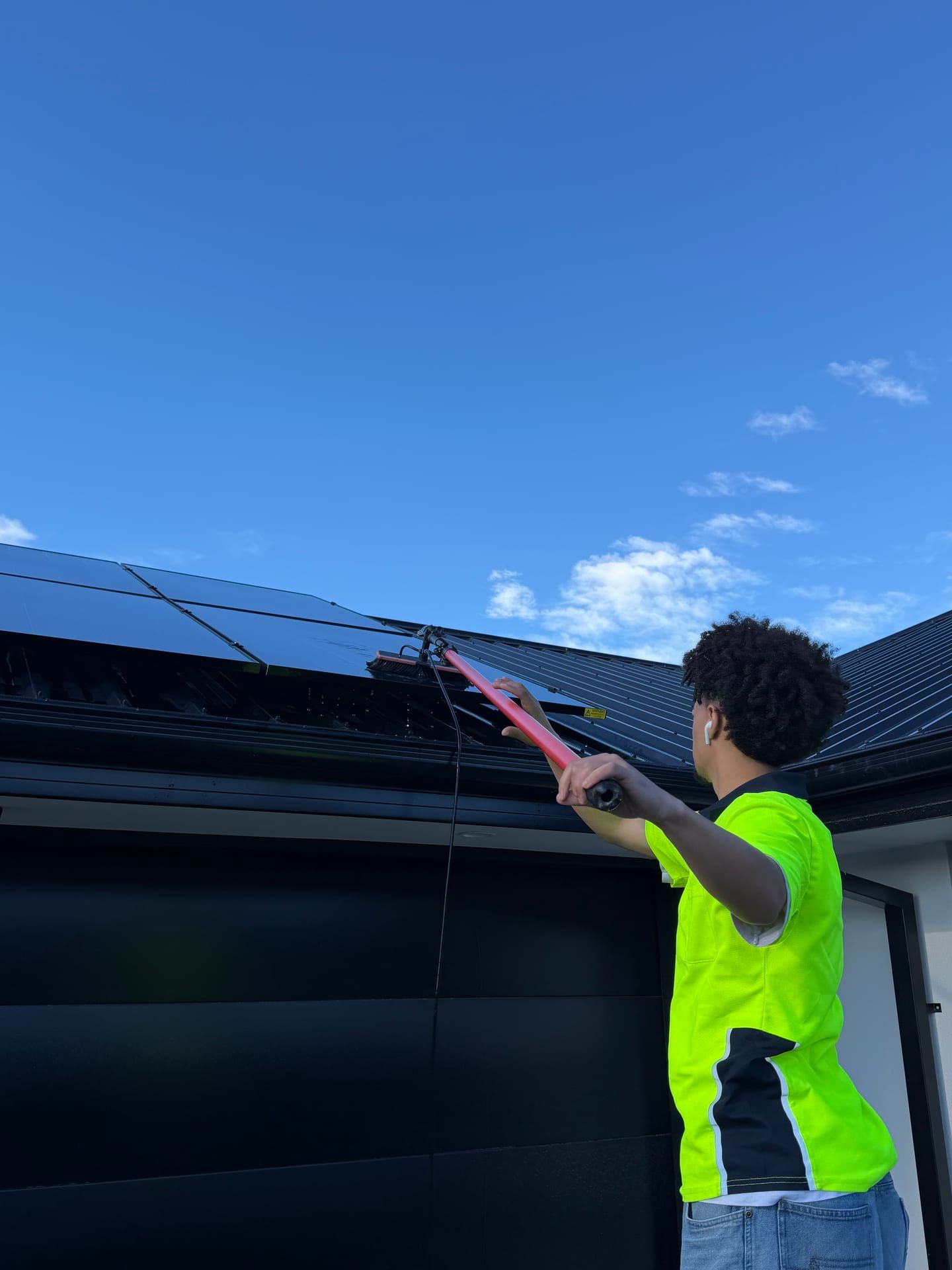 Never Dirty Again team member cleaning rooftop solar panels with a water-fed brush in Christchurch